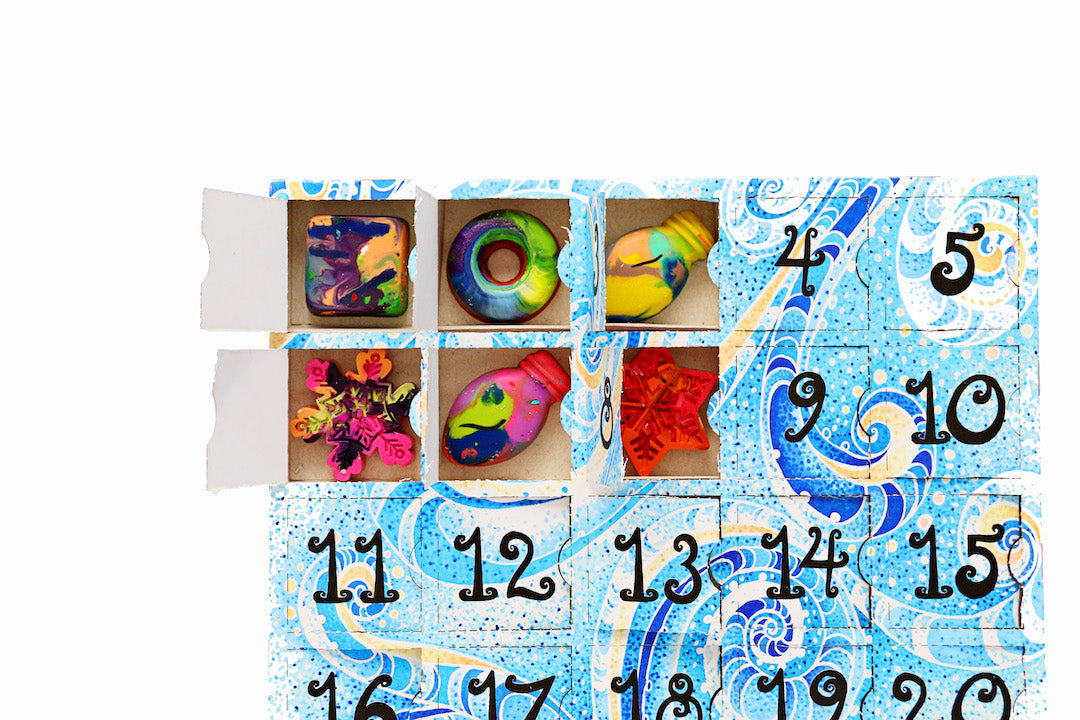 An artistic crayon advent calendar from Art 2 the Extreme® that is blue and whimsical with 25 paper doors and colorful rainbow crayons inside.