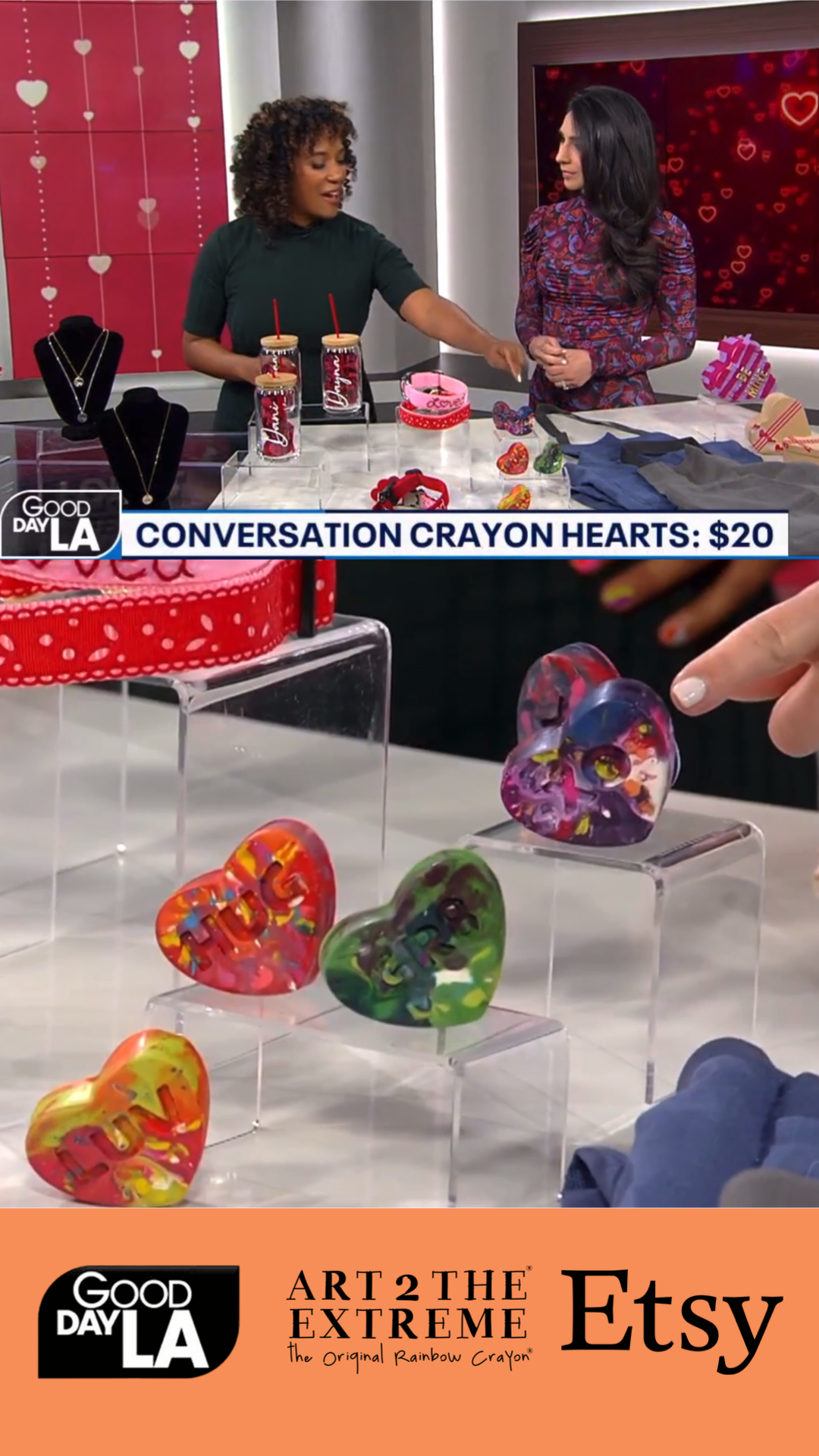 Image of two female TV hosts for Good Day LA showing rainbow crayon kids gifts from crayon shop Art 2 the Extreme on a TV segment. 5 Conversation Heart Crayons are propped on clear plastic display stands to show off cute class valentine ideas.