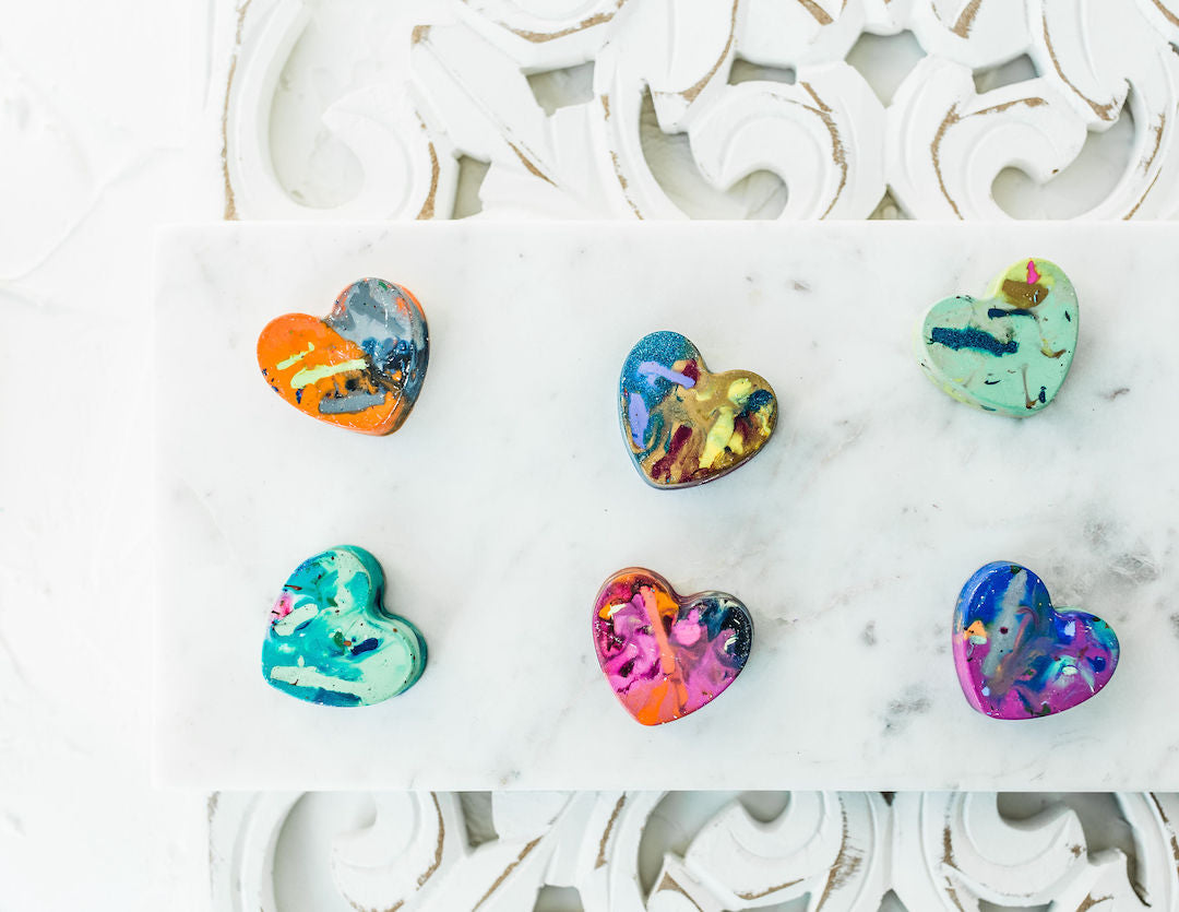 Six heart-shaped crayons in a variety of vibrant, multicolored designs displayed on a white marble surface with an ornate background. Handmade by Art 2 the Extreme, these unique crayons are perfect for Valentine's Day gifts or creative classroom activities