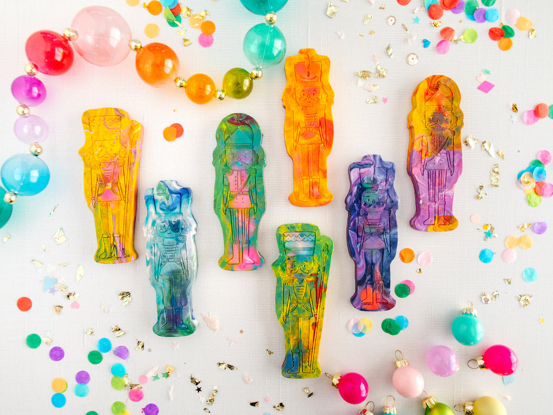 7 Nutcracker rainbow crayons from handmade crayon shop Art 2 the Extreme. Each crayon is shaped like a classic nutcracker figure with vibrant multicolors swirled throughout. The crayon features intricate detailing, including a tall hat, mustache, and uniform-like design, making it a festive and creative holiday gift for children who love crayons coloring page.