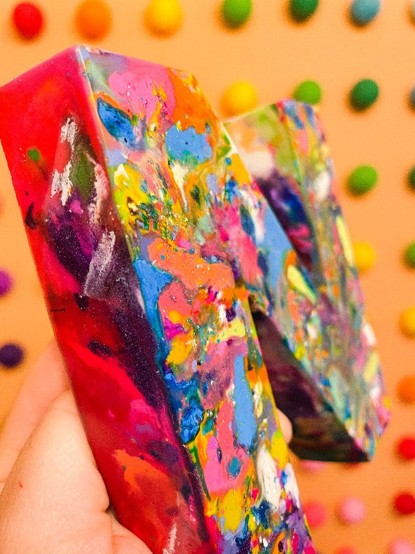 Close up of oversized letter N crayon. Image is of a giant letter N made from recycled crayons from crayon shop, Art 2 the Extreme. This crayon is larger than an adult hand and perfect for back to school gifts or stocking stuffer ideas for the whole family.