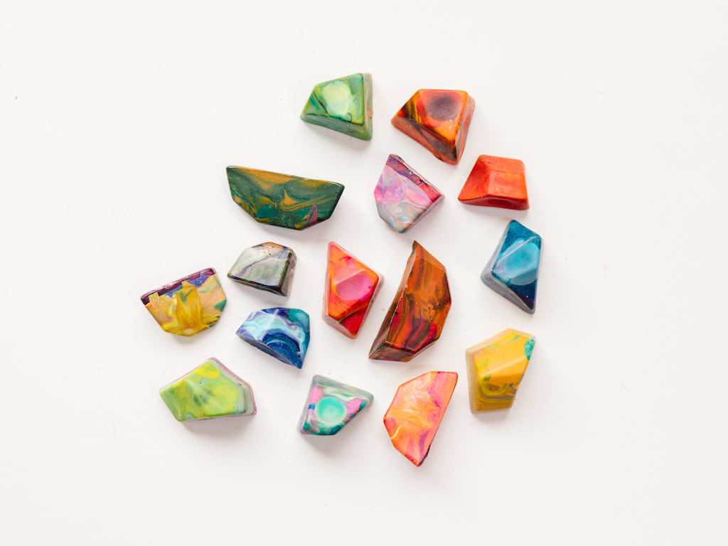 15 multi-colored rainbow rock crayons on a white background. Each crayon rock is shown in a variety of swirly hues that will color with multiple colors when used on a paper. Rocks are mini size and measure about 1-2" in length or width and 1/2" -1" in height. Size varies and the edges are very angular for crayons, making this a great gift for younger kids just learning to hold a crayon.