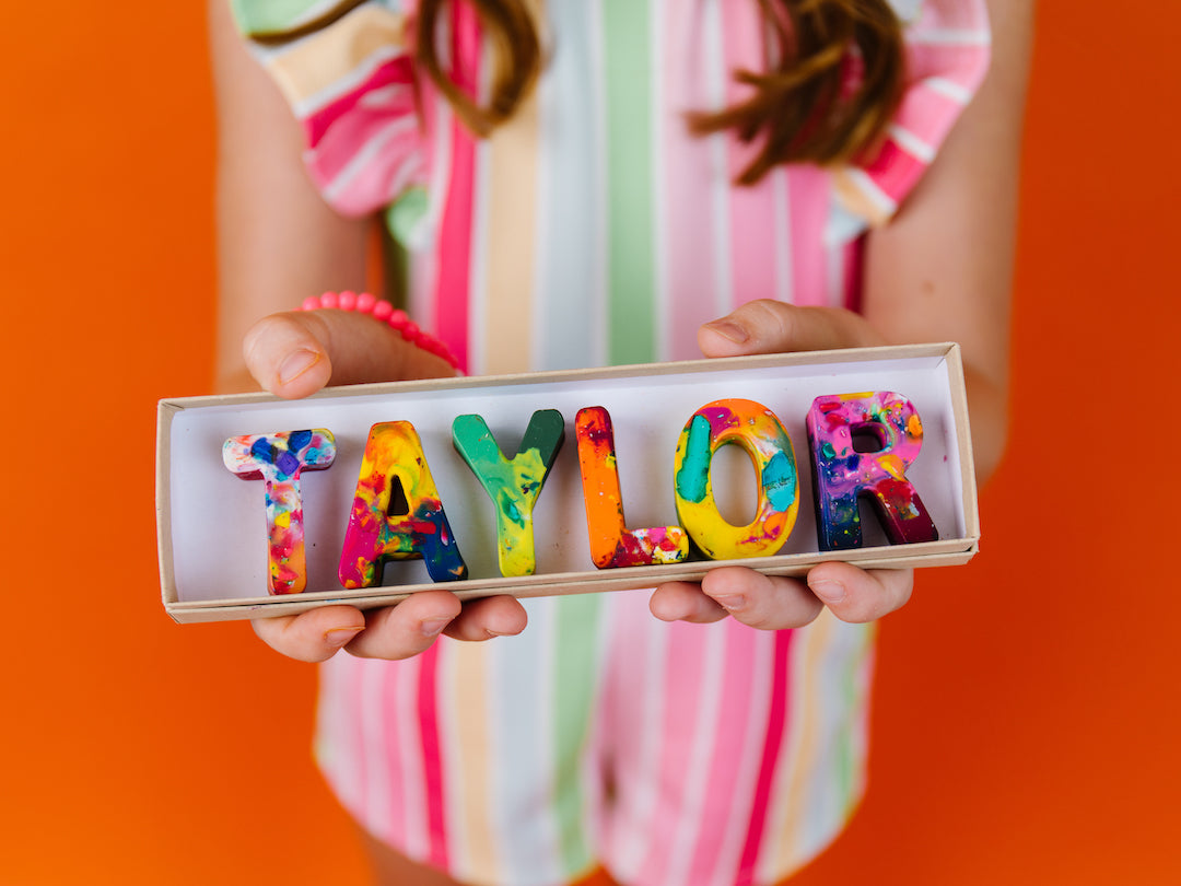 Child holding custom crayon personalized name crayon set in colorful rainbow crayon letters. Multicolored crayon gift for kids, shop letter crayons from Art 2 the Extreme.