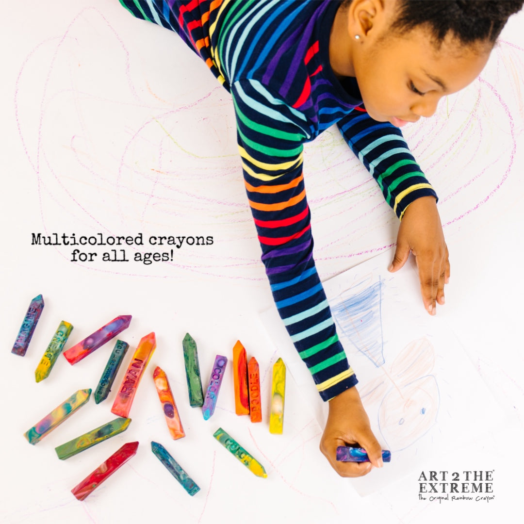 Child holding a rainbow Crayon Stix® from Art 2 the Extreme coloring on a white floor and white paper. Text that reads Multicolored crayons for all ages. 