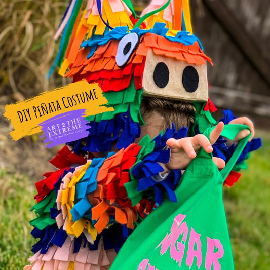 Image of a toddler wearing a rainbow colored pinata costume looking in a green treat bag. Tutorial instructions below for how to create the DIY pinata costume. 