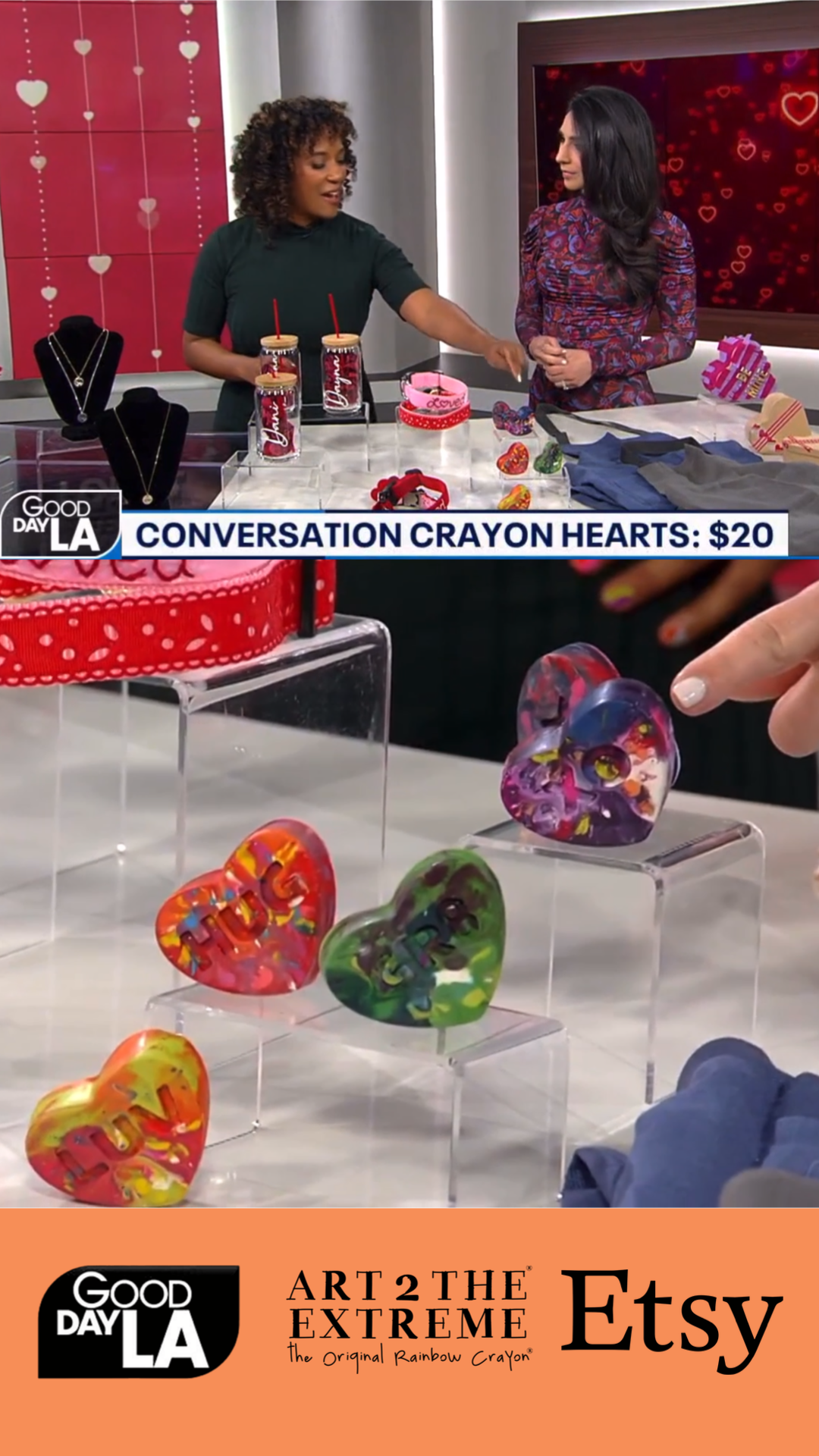 Image of two female TV hosts for Good Day LA showing rainbow crayon kids gifts from crayon shop Art 2 the Extreme on a TV segment.  5 Conversation Heart Crayons are propped on clear plastic display stands to show off cute class valentine ideas. 