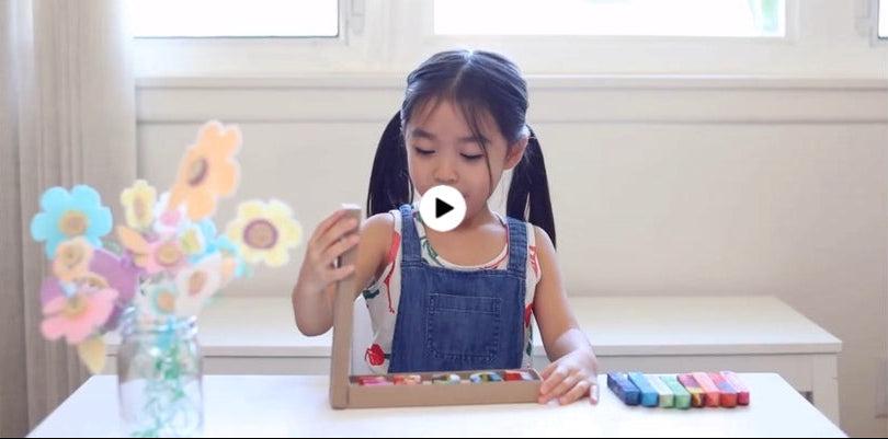 Load video: Child opening a box of customized name crayons that spell LUCIE from crayon shop Art 2 the Extreme®. She colors with the individual letters that spell her name. The crayons color in multi colored lines and swirls. This crayon set makes a great goody bag party favor for kids!