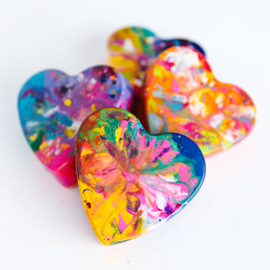 Four Colorful heart shaped jumbo crayons on a white background. Each melted crayon almost looks tie dyed. 