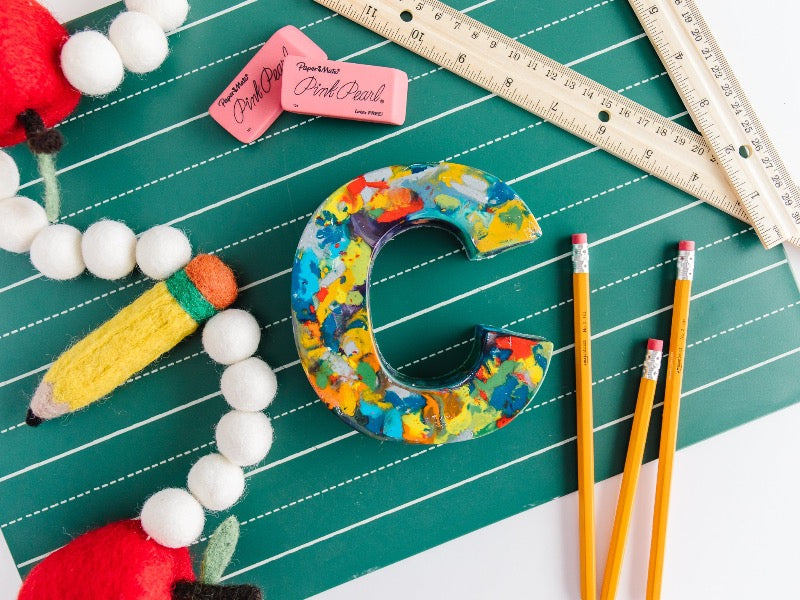 This huge letter C is displayed on a fun lined pages chalkboard pad with pink erasers, rulers, and pencils around it as photo props. Large letter C for crayon themed birthday. This oversized crayon is a perfect crayon gift ideas and a unique back to school kids crayon gift. This letter C decoration can be used as a real crayon and comes in a variety of rainbow crayon colors.  