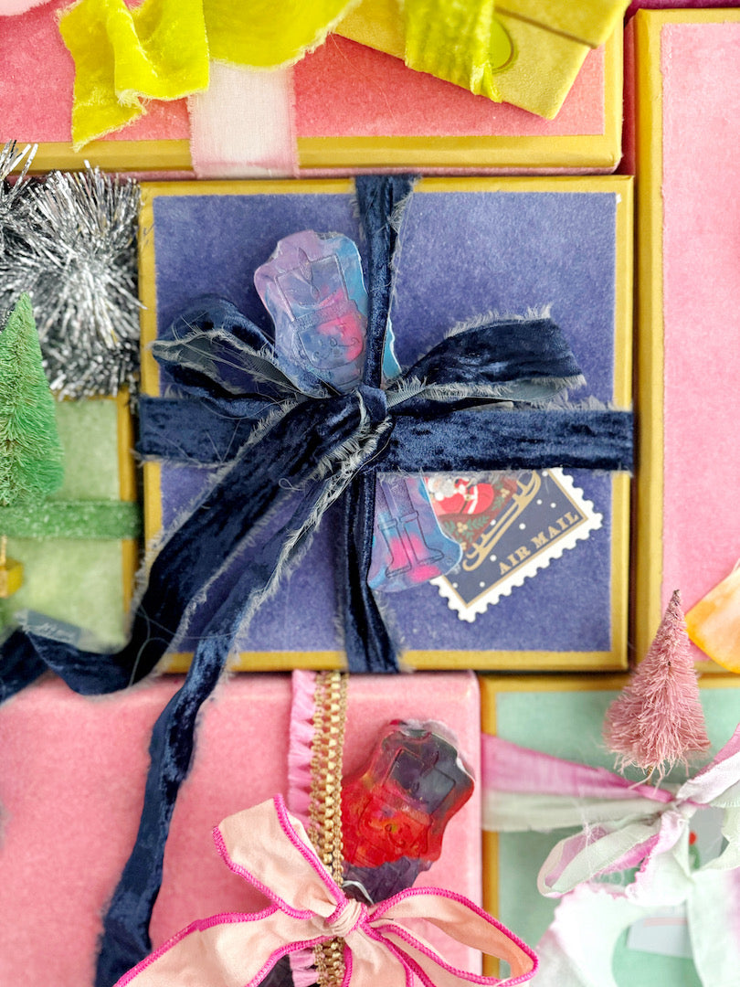 Festive gift boxes wrapped in colorful velvet ribbons and adorned with Art 2 the Extreme® Nutcracker Original Rainbow Crayons® as unique gift toppers, adding a whimsical, holiday touch.